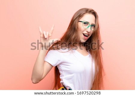 yound blonde woman feeling happy, fun, confident, positive and rebellious, making rock or heavy metal sign with hand