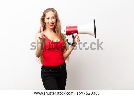 yound blonde woman smiling proudly and confidently making number one pose triumphantly, feeling like a leader holding a megaphone