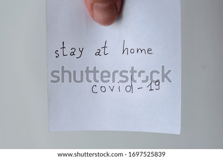 inscription stay at home covid-19 on paper, finger holds sticker