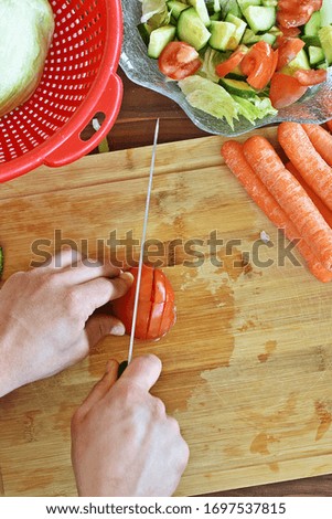 Picture from above - a man cuts a tomato for a salad - delicious, fresh, organic tomato on a wooden board, for a fresh, delicious, healthy salad