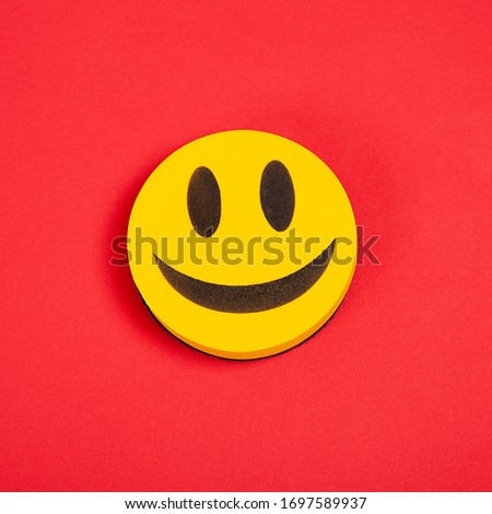 Yellow three-dimensional smile on a red background. Funny look. Happiness, joy, luck, success in business.
