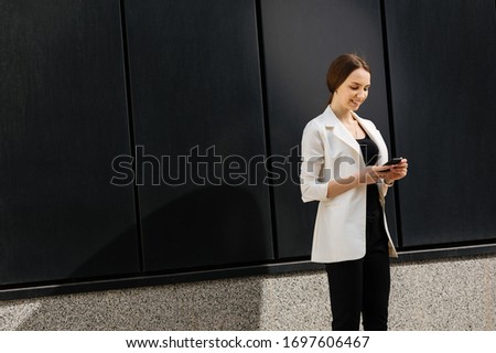 Photo of smiling businesswoman in white blazer , talking on the phone, outside
