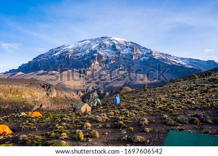 Camping on mount Kilimanjaro in tents to see the glaciers in Tanzania, Africa Orange tents on the way to Uhuru Peak. Royalty-Free Stock Photo #1697606542