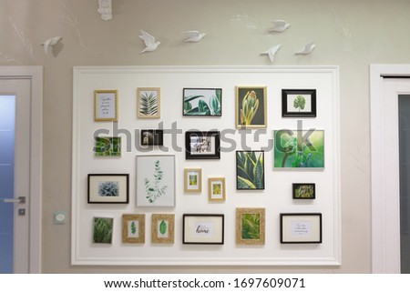 Many photo frames are hanging on the wall. Frames between two interior doors. The wall is decorated with plaster figures of birds. In beige tones.
