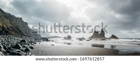 Panoramic view on the Atlantic Ocean and rocks on the Benijo beach shore of volcanic black sand in a cloudy golden sunset