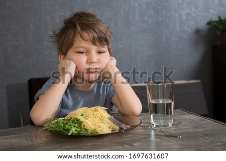 The child doesn't want to eat. The boy eats spaghetti. Poor appetite. Healthy diet. Refuses to eat. A disgruntled child at lunch. Royalty-Free Stock Photo #1697631607
