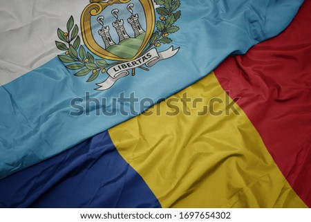 waving colorful flag of romania and national flag of san marino. macro