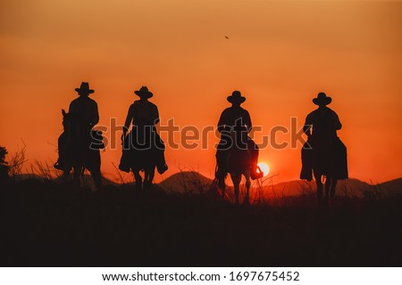 Silhouette the cowboy riding on a mountain with an yellow sky.