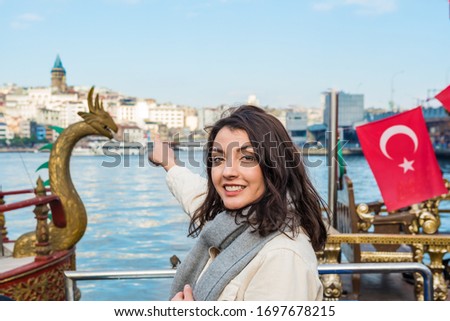 Beautiful woman in fashionable modern clothes shows popular Galata Tower with Golden Horn view at background in Istanbul,Turkey