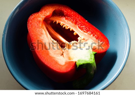 half a red sweet pepper is in a blue salad bowl on a gray background