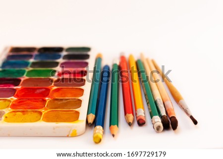 Watercolor paint, brushes, pencils well used on white background. Back to school, home schooling concept