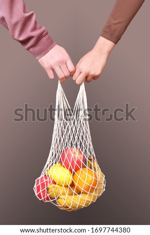 A shopping bag with necessary products rich in vitamins in the hands of a man and a woman during quarantine. On dark background. The concept of a friendly family when overcoming difficult