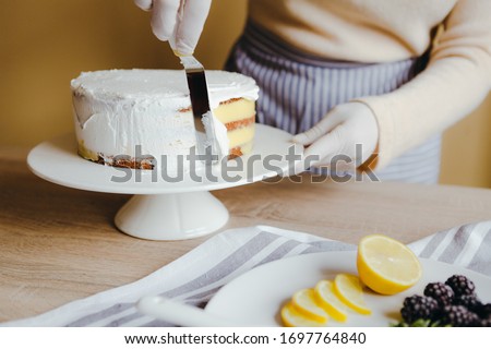Woman housewife spreading the icing to cover the top of the cake. Housewife smoothing surface using spatula, close up cropped photo. Free time on quarantine.