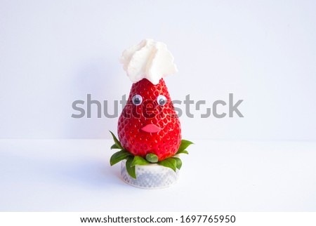 Funny srawberry with face and hat from cream. Creative food background.