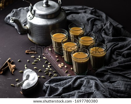Indian chai in glass cups with metal kettle and other masalas to make the tea.  Royalty-Free Stock Photo #1697780380
