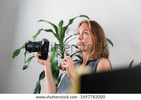 Freelance. A young woman is holding a camera and thinking about ideas for work. Indoor plant in the background. The concept of self-isolation, quarantine and remote work