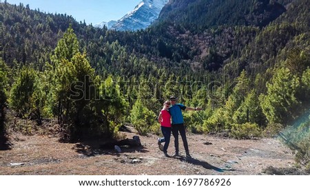 A couple in hiking outfits standing on the trekking trail and posing for the picture in Himalayan valley, along Annapurna Circuit in Nepal. They are happy and full of energy. Cheerful moments