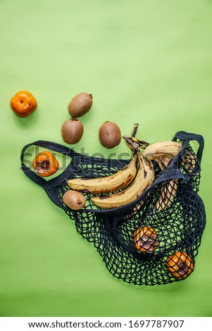 Vintage black reusable eco friendly string bag. Inside are ripe bananas, persimmons, kiwi. The concept of recycling, environmental protection,naturalness.Greenish background. Copy space. Vertical view