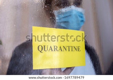 Quarantined lonely man with covid-19 home insulation. Yellow warning sign with text Quarantine in window. Coronavirus pandemic prevention. Man in protective medical mask stay at home. Medicine concept