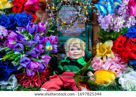boy doll holding tulip sitting in green grass surrounded by spring flowers