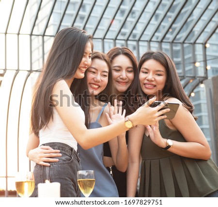 group of young women friends having fun looking at something funny on their smart phone and laughing while having party on rooftop night club