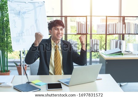 happy young asian businessman with success and gladness concept sitting on chair in modern computer workplace.