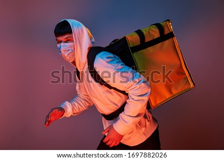 delivery man in white clothes with a yellow backpack on a colored background run
