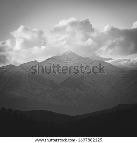 Conceptual black and white image of the brightened mountain peak , white clouds and dark forest in the forehand. Concept of hope; tranquility and balance.