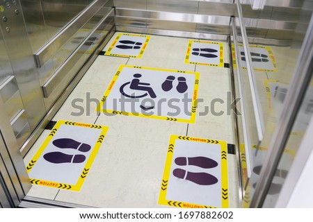 View of footprint sign for stand in lift. Social distancing with COVID-19 coronavirus crisis.yellow footprint sign with text caution social distance, Social distancing the elevator (Lift) in hospital.
