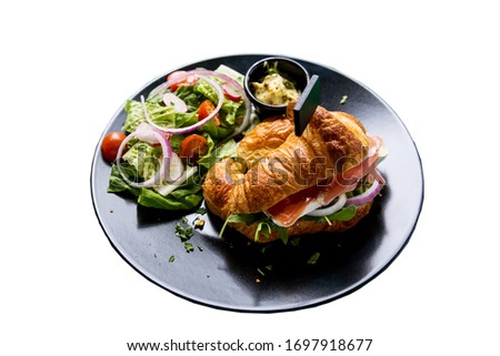 Croissant sandwich with smoked salmon, brie and onion. Salad included. Isolated over white background.