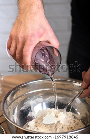 Man's hand pouring the water into a bowl. Kneading the dough for pizza Royalty-Free Stock Photo #1697918845