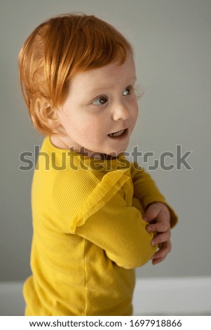 Cute red-haired toddler girl posing to camera on a grey background