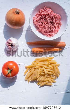 Ingredients for pasta bolognesa: macaroni, minced meat, carrot, onion, garlic and tomato on textured white background. Italian cuisine. Flat lay. Vertical picture.