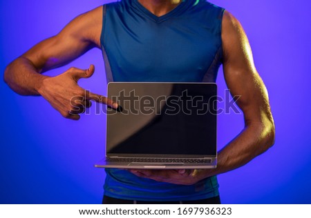 Online Workout. Fitness Guy Showing Laptop Empty Screen Standing On Blue Studio Background. Cropped, Mockup