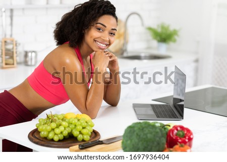Cooking With Some Help. Afro girl in red sports bra posing with personal computer in loft kitchen, copy space