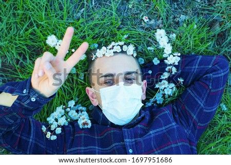 medical mask as protection against coronavirus. guy lies on grass around early spring flowers