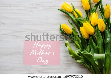 Happy mother's day text sign with bouquet yellow tulips on white rustic wooden background. Greeting card with flowers concept. Holiday greeting card for Mother's Day! Top view, flat lay.