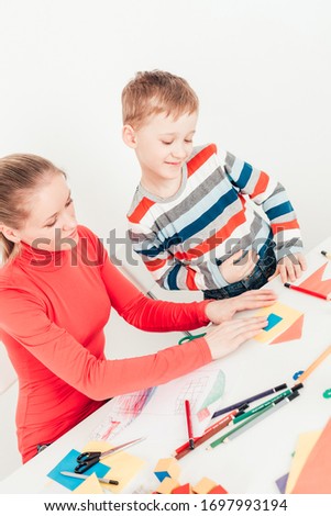 Mother with little son doing application paper picture from colored papers