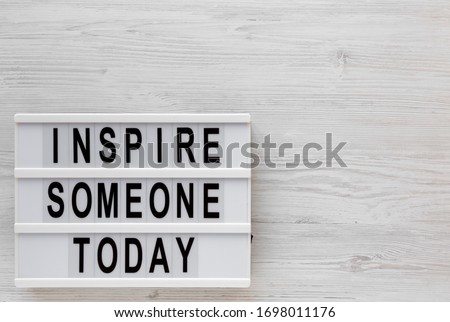 'Inspire someone today' words on a lightbox on a white wooden background, top view. Overhead, from above, flat lay. Copy space.