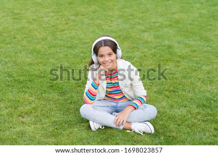 Make It Happen. Listen music while relaxing outdoor. Kid girl enjoy music green grass meadow. Pleasant time. Child headphones listen music. Cool girl headphones listening music. Educational podcast.