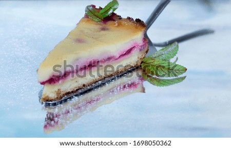 Slice of raspberry and  custard cream cake, decorated with mint leaves, with a light blue background 