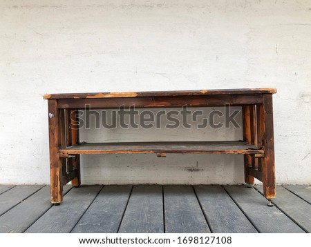 Old vintage table woodcraft furniture are unbalanced legs on dust wooden floor in house. Table near plaster wall outside house. Memory furniture item house with family and work in house.