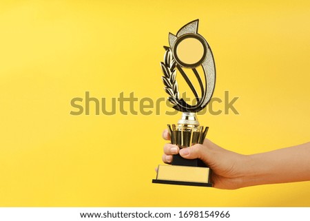 Hand holding a golden trophy on yellow background