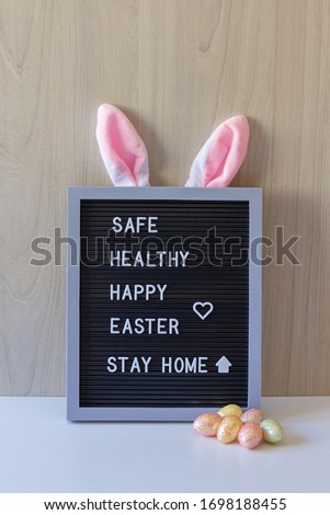 Decorative sign with bunny ears and colored eggs in front with the easter message: Safe, healthy, happy easter, stay home.