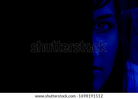 Art photo depicting half the face of a girl with a blue face and a serious look and a black background with free space for text.