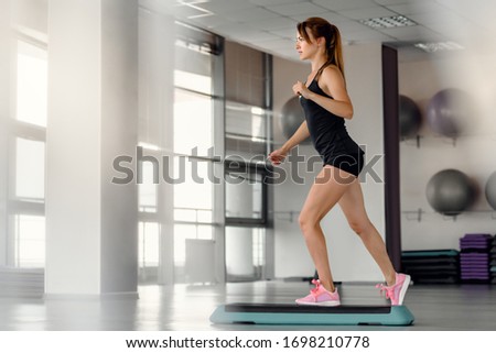 Slim athletic woman doing aerobic with stepper in modern gym