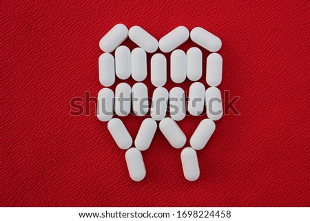 Tooth from pills on a red background. Dental clinic concept. Calcium vitamin in the form of a tooth spilled out on a red background.