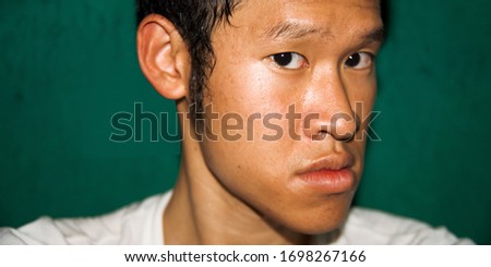 A face of an Asian man looking suspicious and a little scared. He gives 45 degrees angle to the camera. His jaw protrudes. He has an underbite, on green background Royalty-Free Stock Photo #1698267166