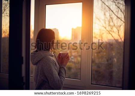 Woman near window at sunset in isolation at home for virus outbreak. Stay home concept. Royalty-Free Stock Photo #1698269215