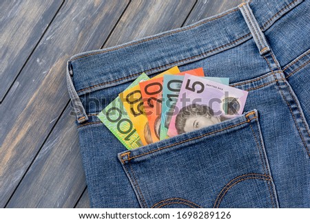 Australian bank notes in light blue jeans pocket against a wooden background.